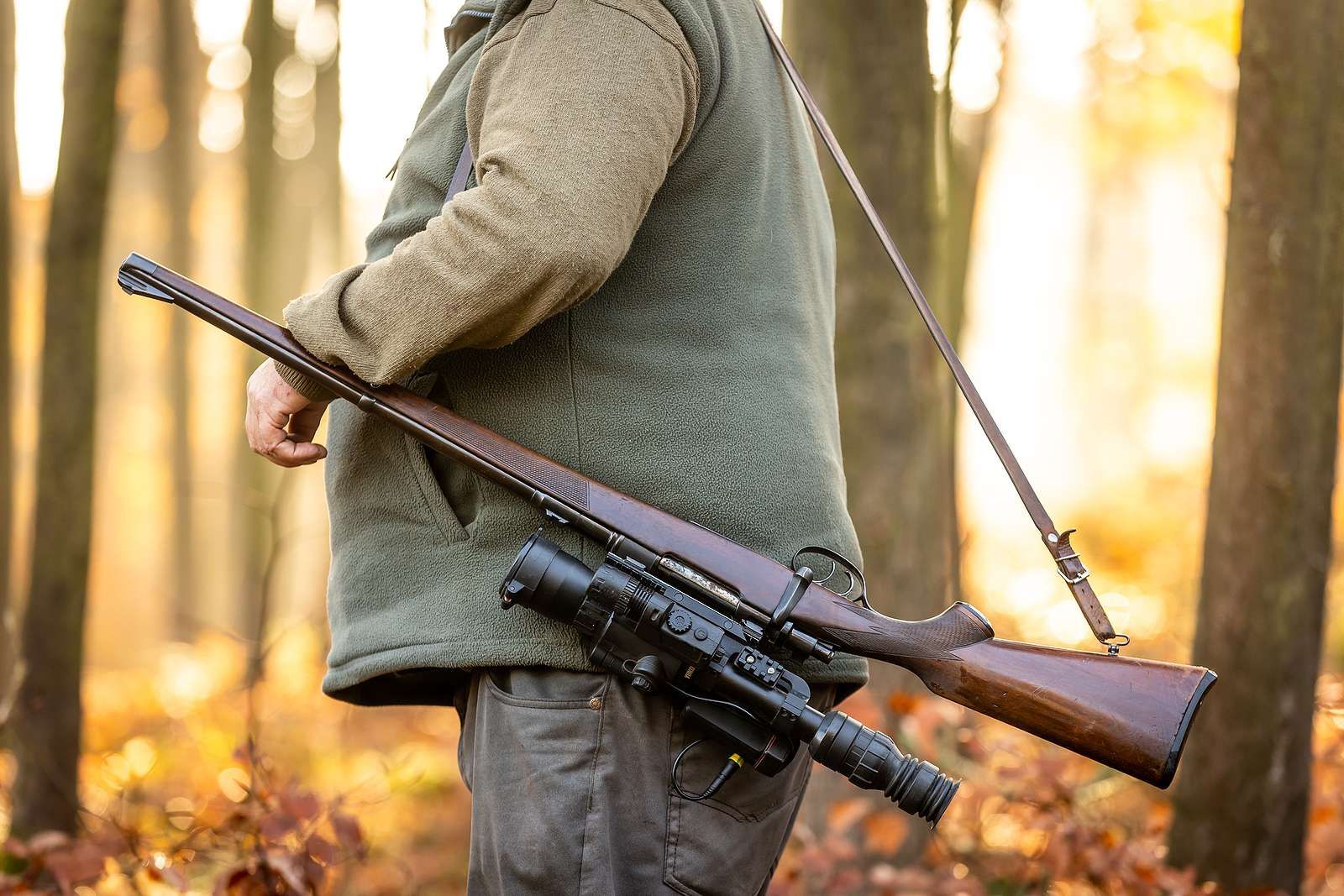 Hunter holding a rifle in an autumn forest, with another rifle slung over the shoulder