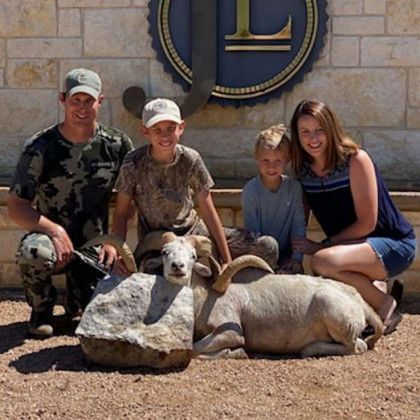 Group posing with a resting ram and a large rock in front of a circular sign outdoors.