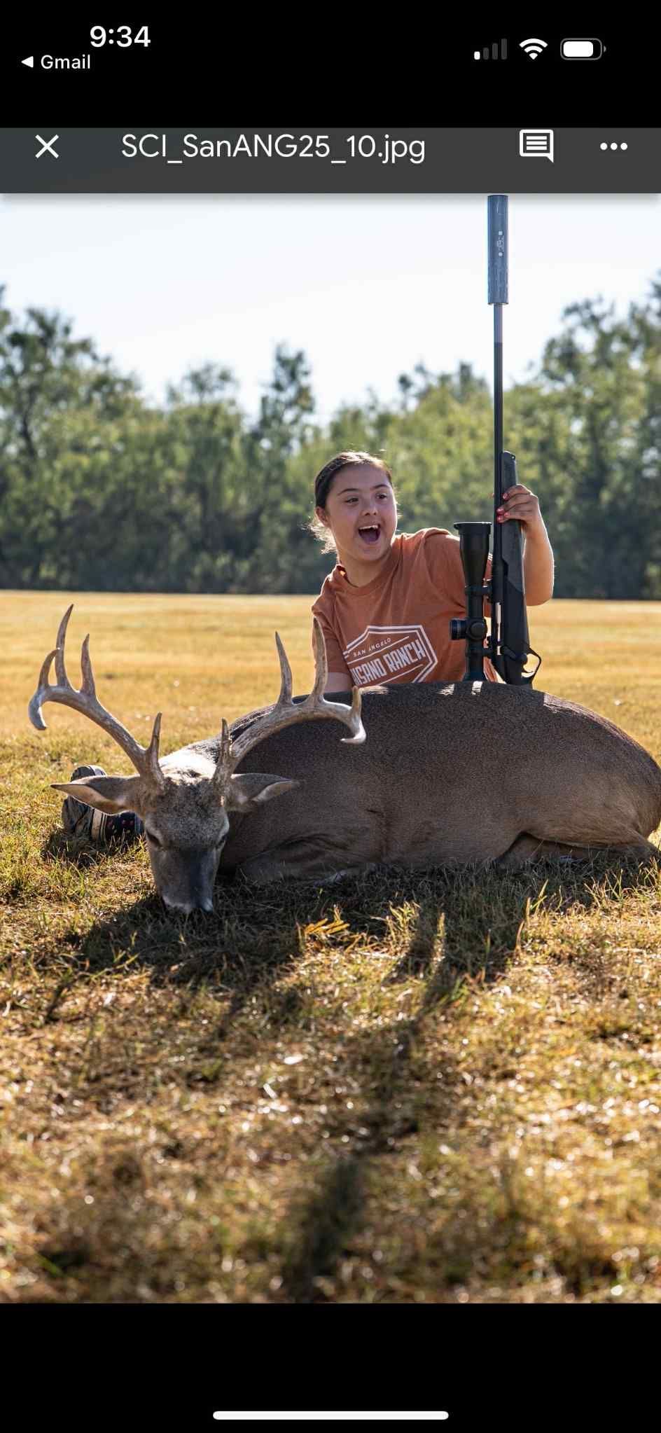Person sitting on a large deer in a sunny field with a rifle behind them