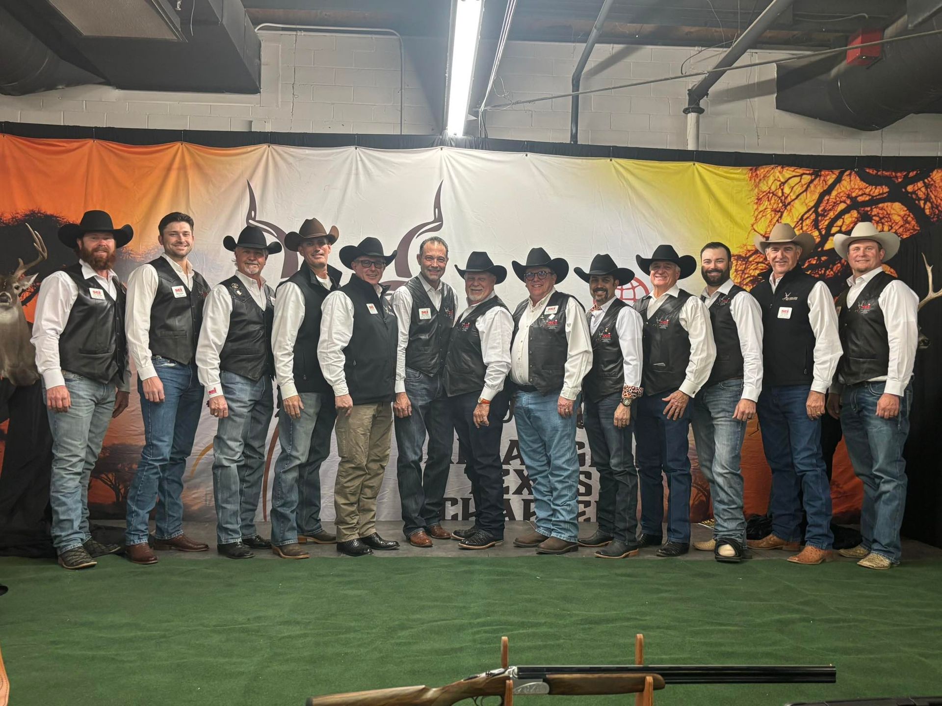 Group of people in cowboy hats and vests standing in a line at an indoor western-themed event.