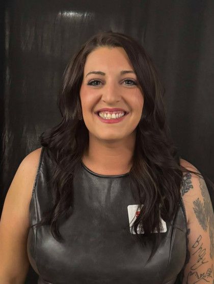 Smiling woman with long dark hair in a black sleeveless top against a dark background
