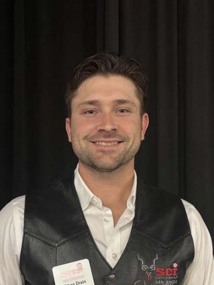 Smiling man in white shirt and black vest standing against a dark backdrop.