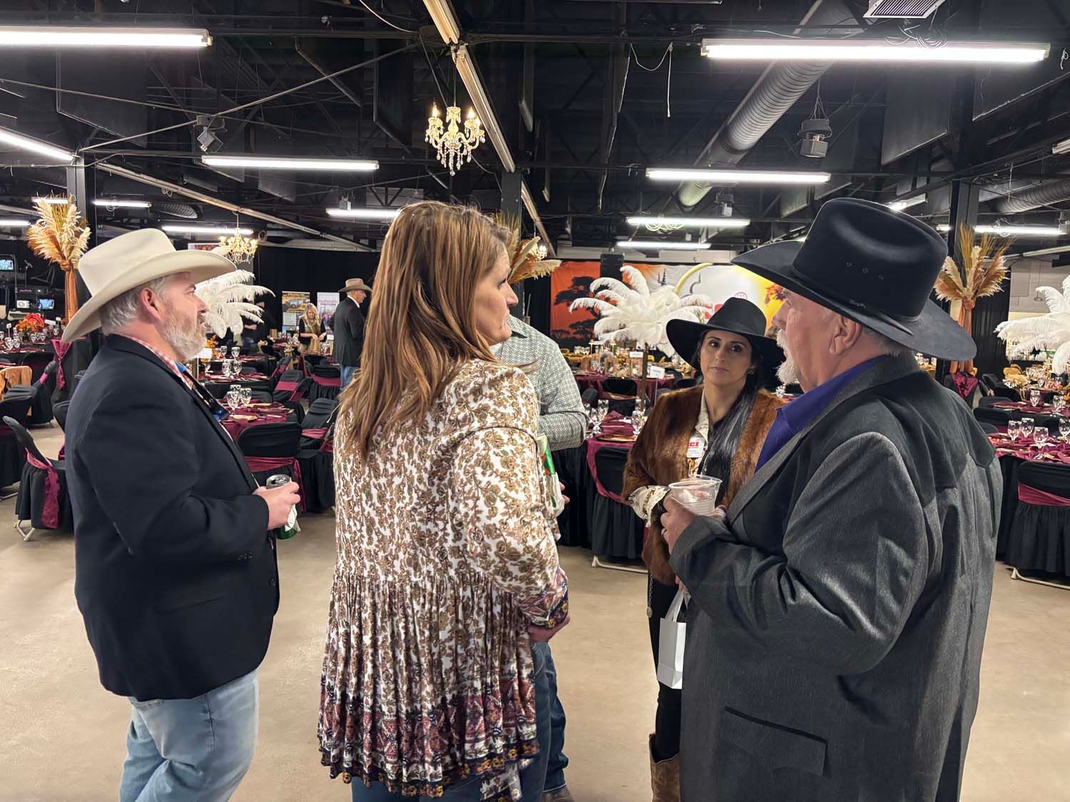 People chatting in a clothing market, with hats and racks of apparel in the background.