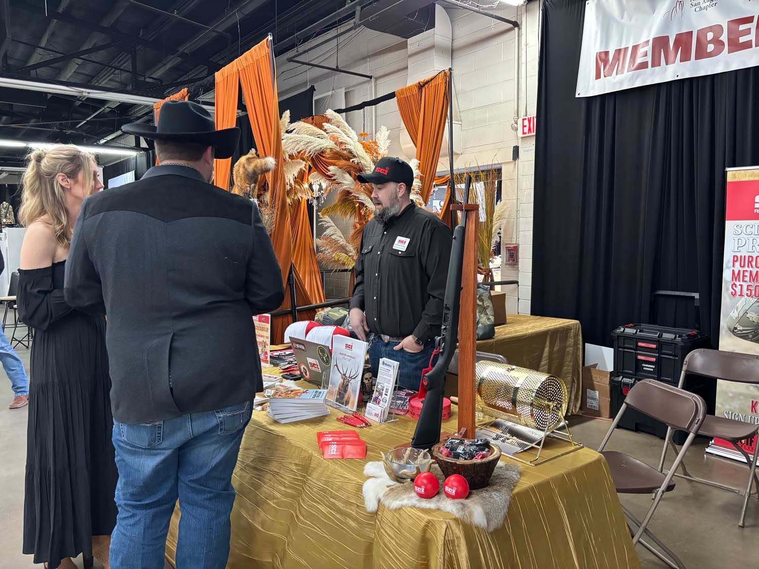 Vendor booth at an indoor market, with people browsing handmade items and a table of crafts under black drapes.