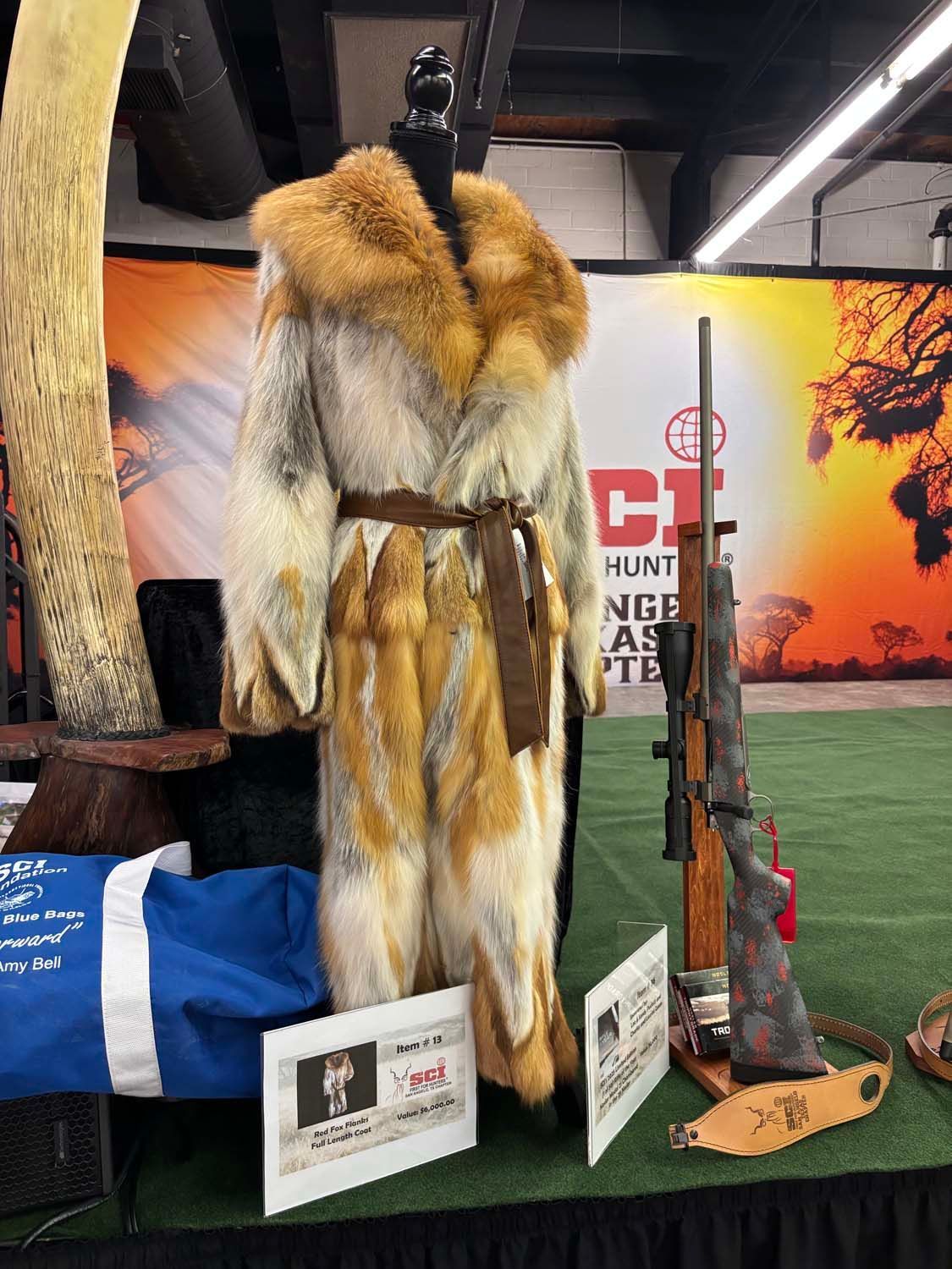 Museum display of a fur coat and rifle in front of a hunting-themed backdrop