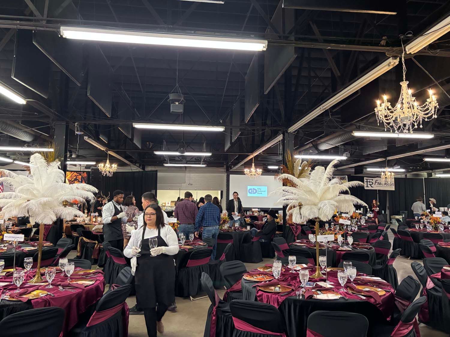 Banquet hall with round tables, black and magenta decor, chandeliers, and a server walking through the crowd