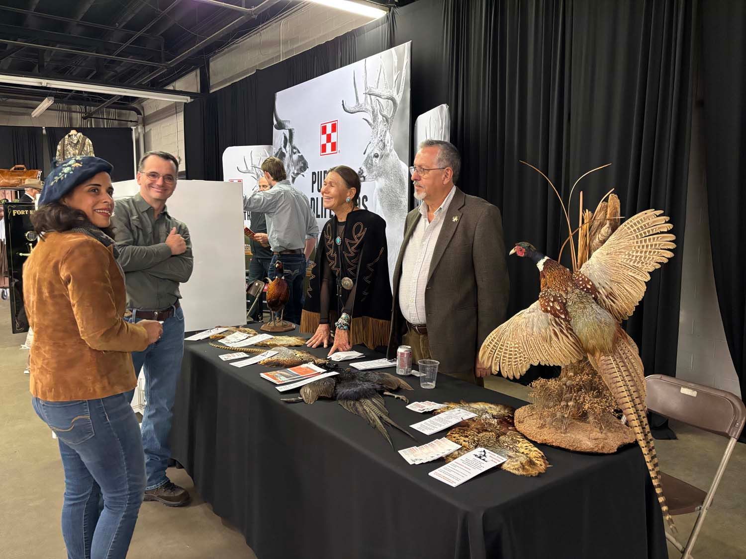 People browsing an art display at a table, with a large bird sculpture on the right.