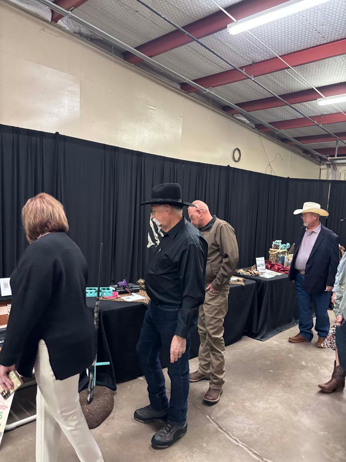People browsing tables at an indoor event under black drapes and a metal ceiling.