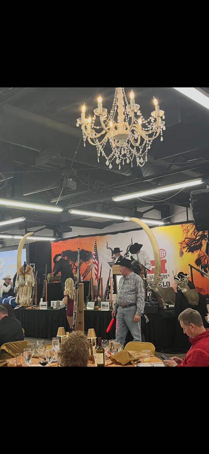 People browsing a colorful indoor market booth under a chandelier, with hanging clothes and artwork behind them