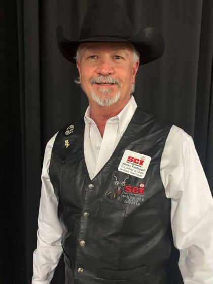 Man in black cowboy hat and leather vest, smiling in front of a black curtain.