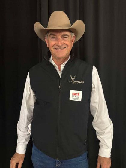 Smiling man in cowboy hat, white shirt, and black vest against a dark backdrop