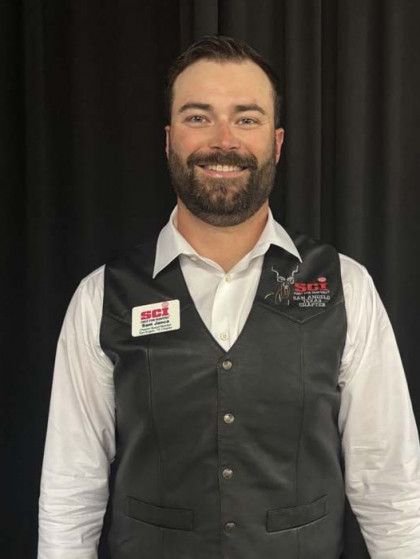 Smiling person in a white shirt and black vest standing before a black backdrop