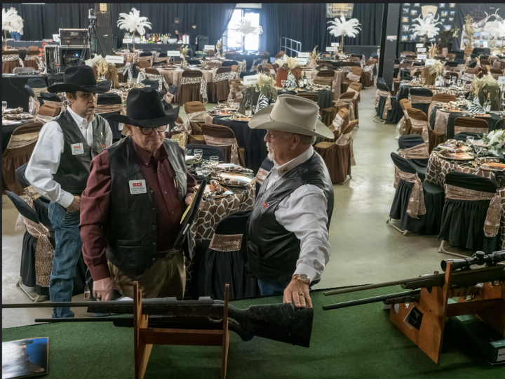 People in cowboy hats browsing saddles and tack at an indoor western gear market