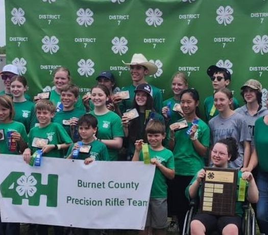 Burnet County Precision Rifle Team group posing with green 4-H banner at district event