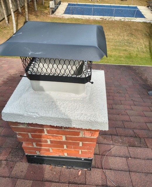 Brick chimney with black metal cap on a shingled roof in a backyard.