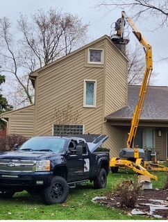Black pickup and crane lift worker to repair roof on a beige house