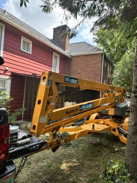 Yellow construction lift beside a red house in a backyard under trees