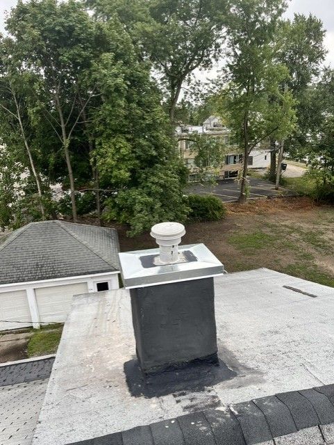 Rooftop chimney vent on a flat gray roof, with trees and houses in the background.