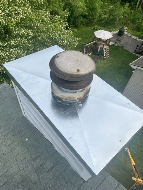 Rooftop vent pipe on a silver metal roof with green trees and patio furniture in the background