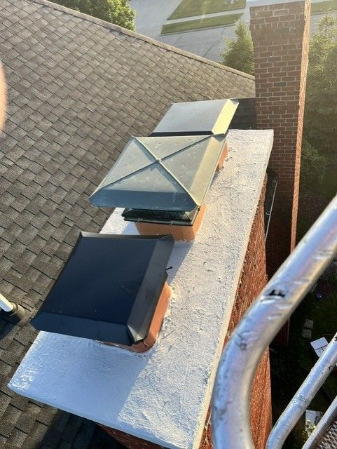 Roof vents and a chimney on a sloped shingle roof beside a metal ladder or railing.