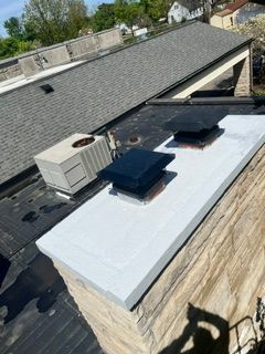 Flat rooftop with white membrane, black vents, and HVAC unit beside a shingled roof.