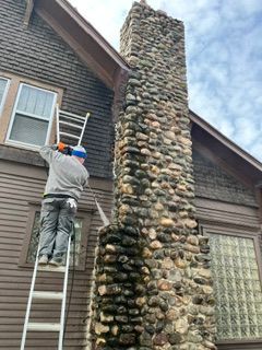 Person on a ladder painting a tall stone chimney on a house