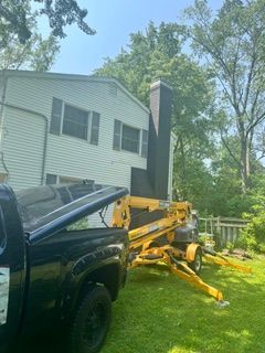 Yellow excavator beside a black pickup in a grassy yard next to a white house