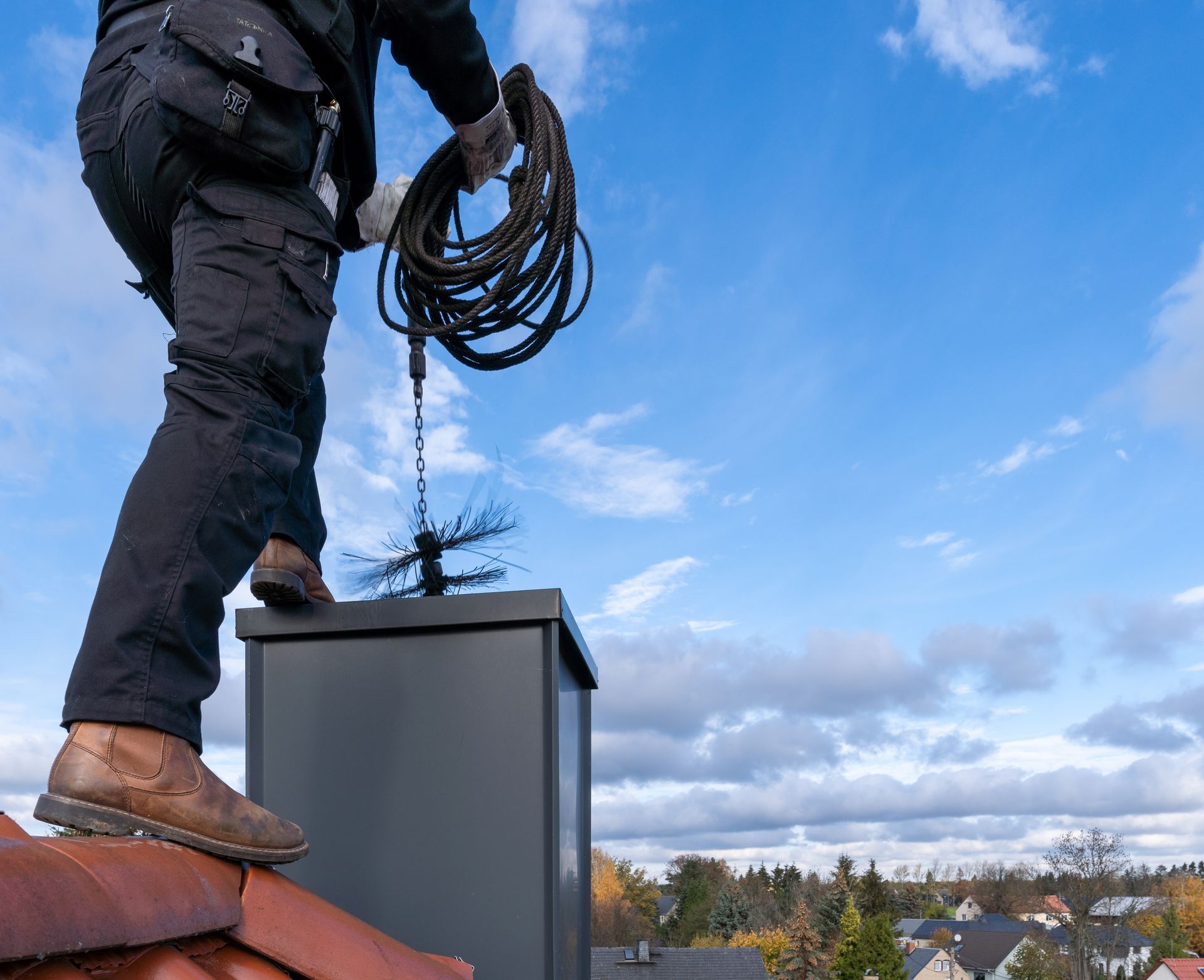 Worker on a rooftop holding a coiled cable beside a chimney under a blue sky