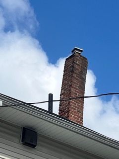 Brick chimney above a white roof against a blue sky with clouds