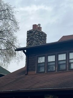 House roof with a stone chimney and dormer windows under a cloudy sky