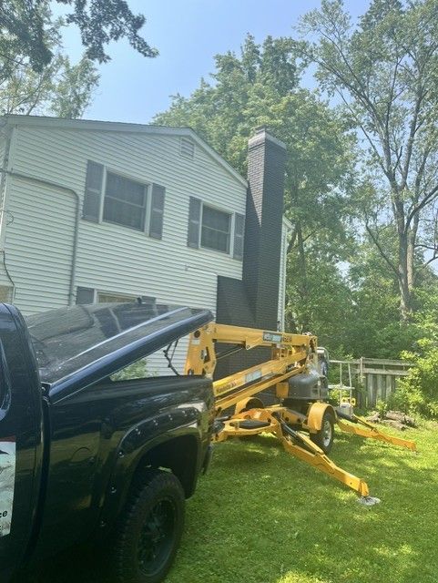Black pickup beside yellow lawn mower tipped on grass near a house and trees