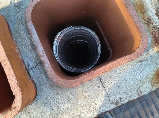 Black corrugated pipe inside a square terracotta drain opening outdoors