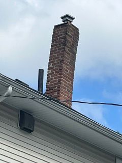 Brick chimney on a house roof against a blue sky.