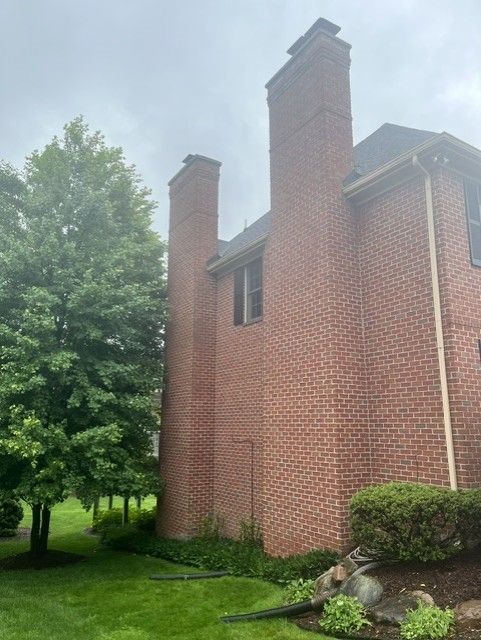 Red brick house exterior with two tall chimneys, green lawn, and trees on a foggy day