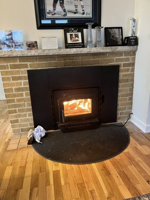 Lit wood stove in brick fireplace with hardwood floor and decor on the mantel.