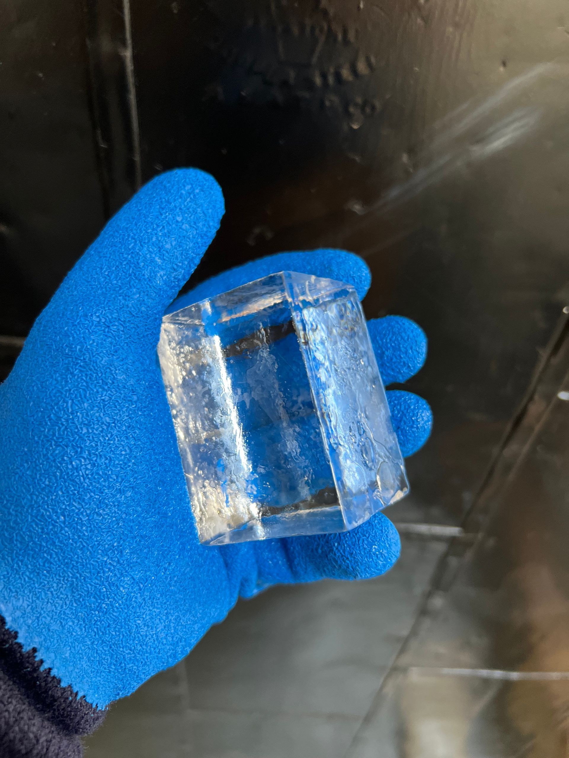 Blue-gloved hand holding a clear rectangular block against a dark background