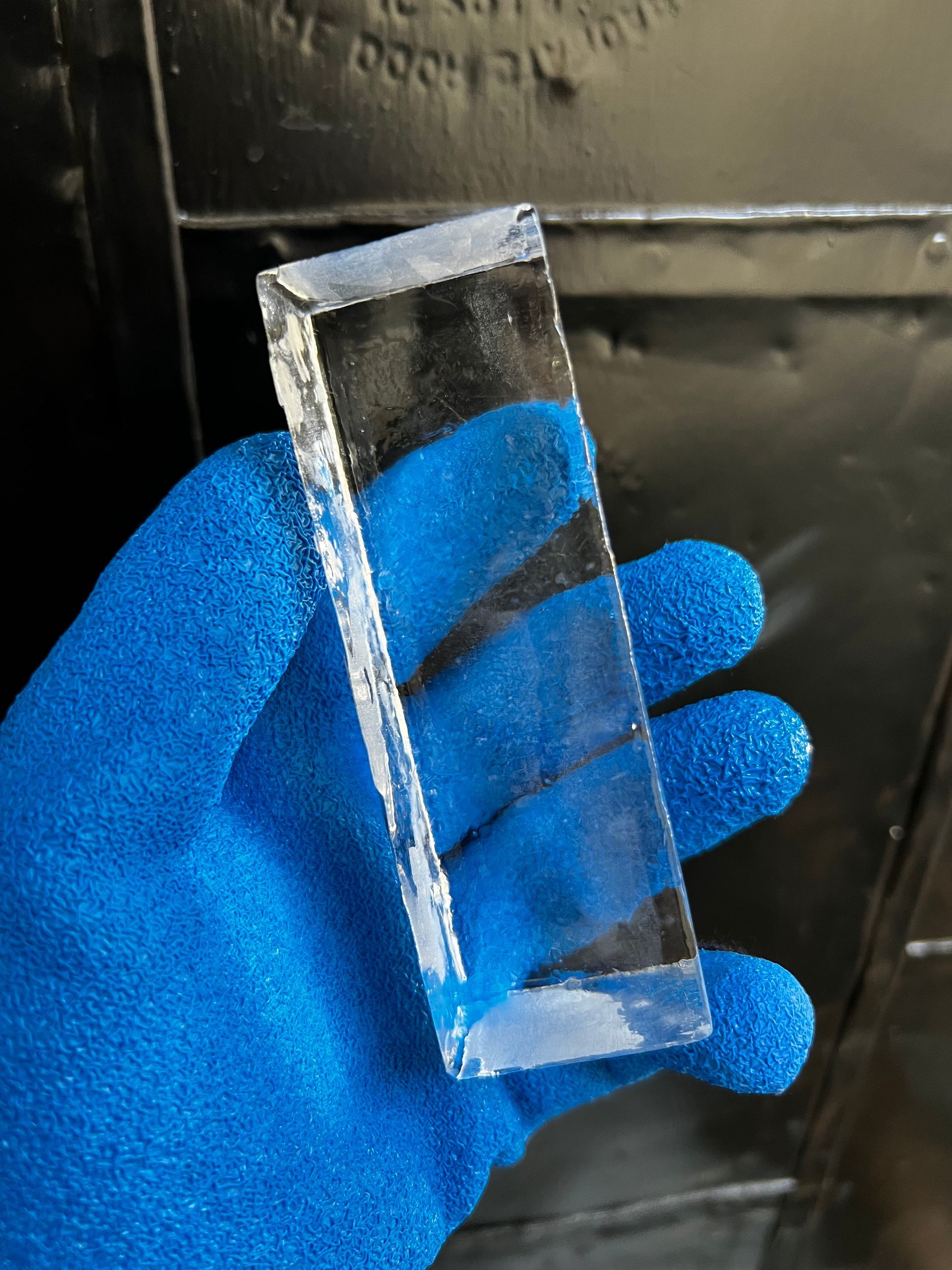 Blue-gloved hand holding a clear rectangular glass piece against a dark background