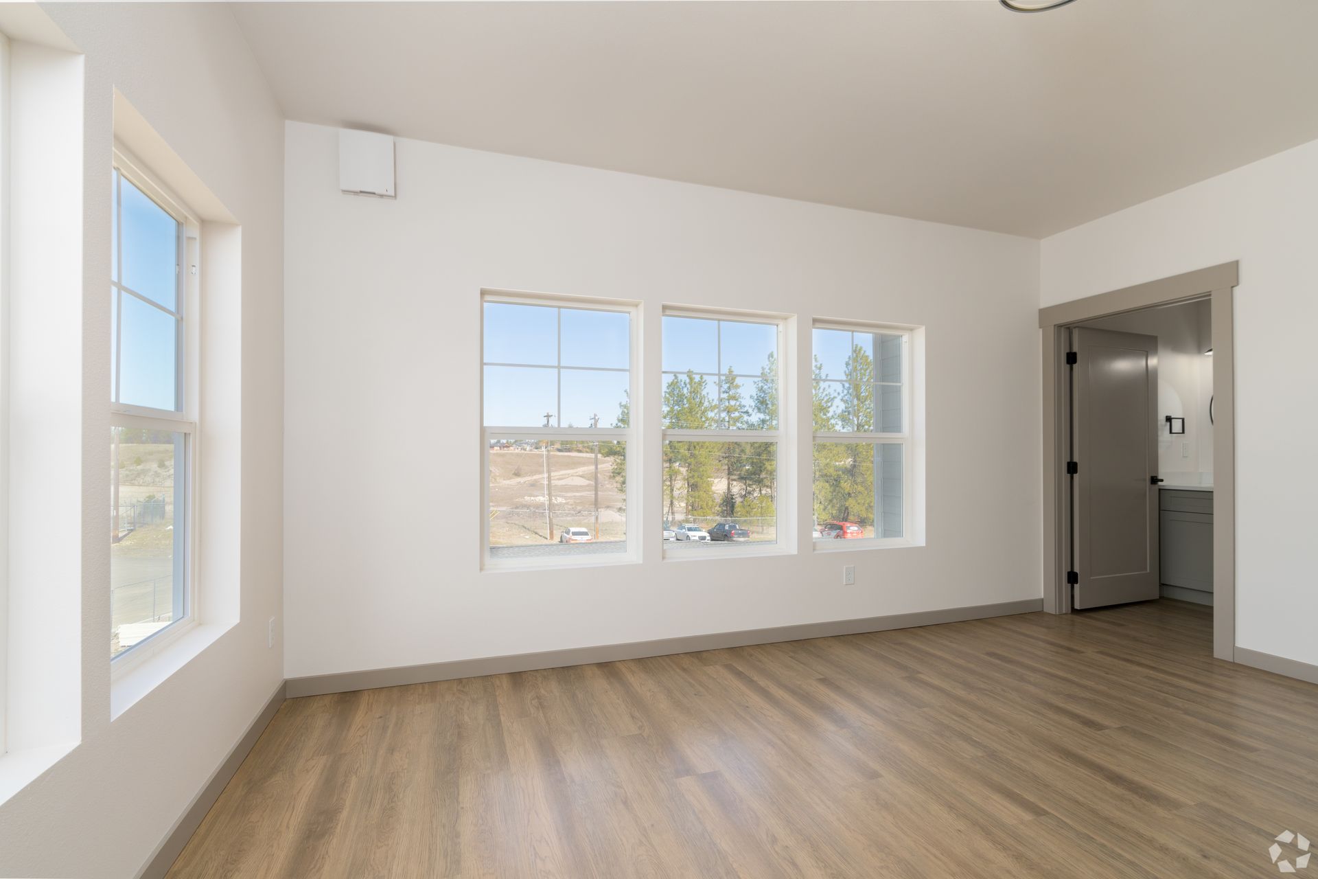 An empty living room with hardwood floors and lots of windows.