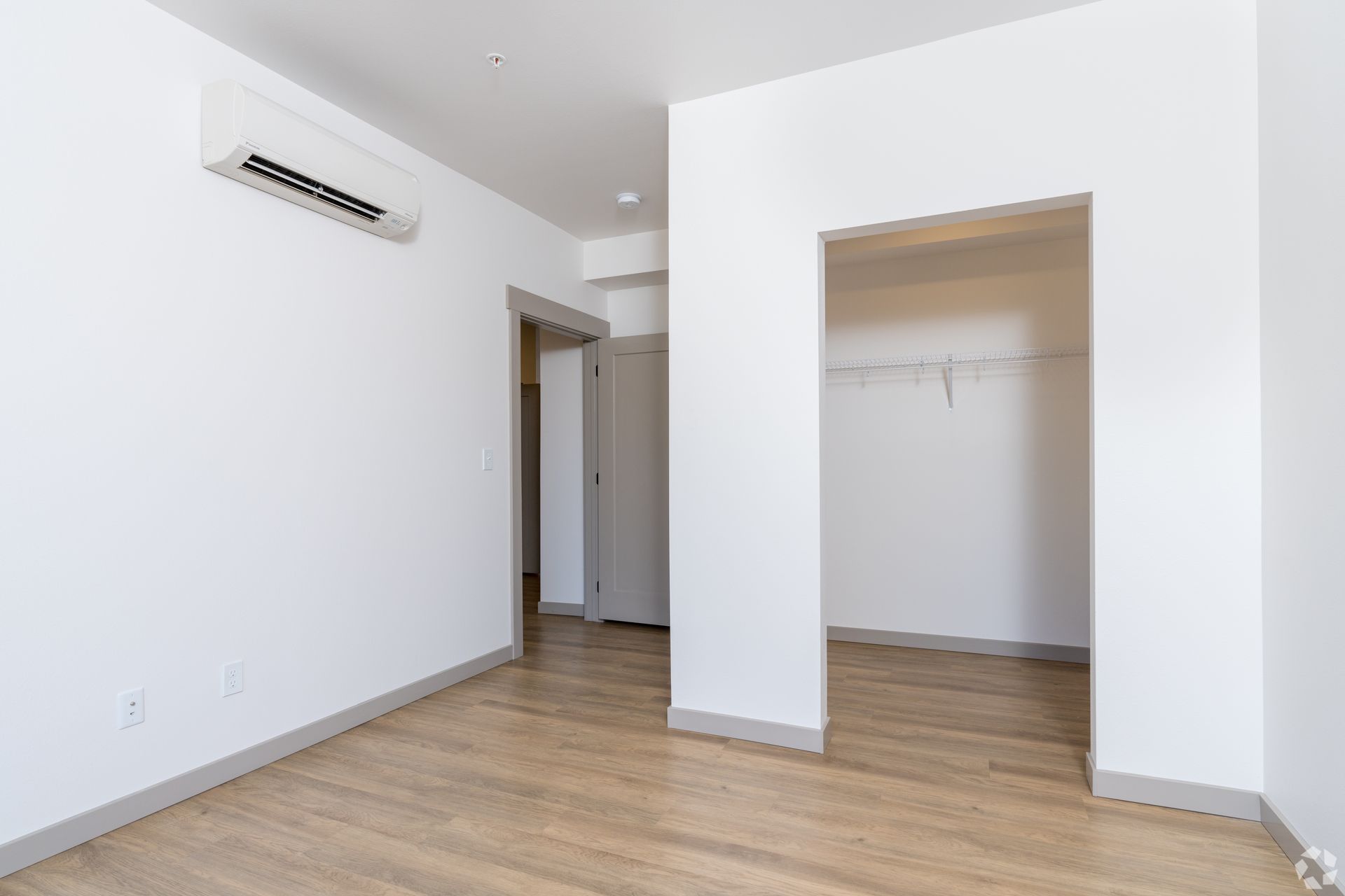 An empty bedroom with hardwood floors , white walls and a walk in closet.