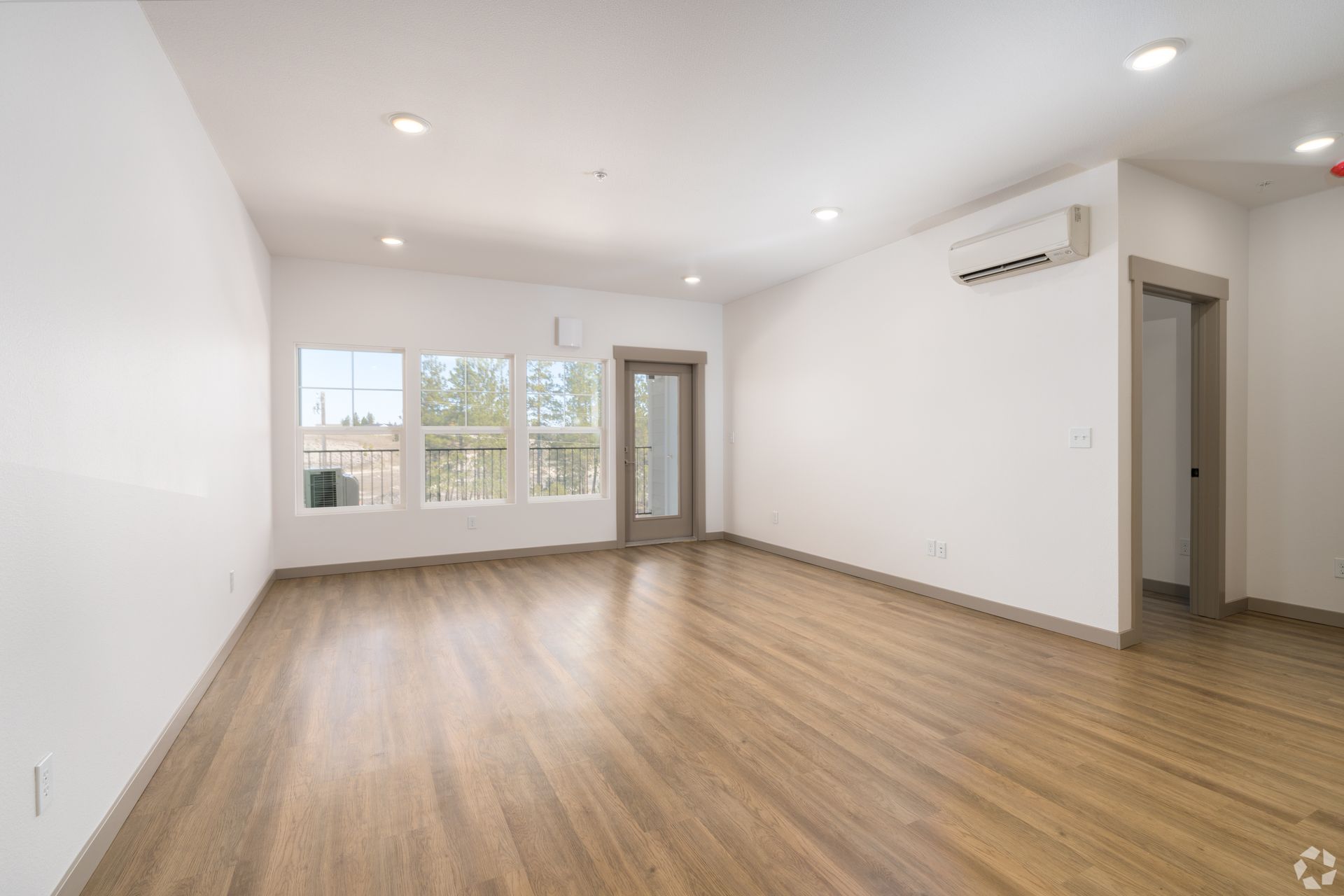 An empty living room with hardwood floors and white walls.