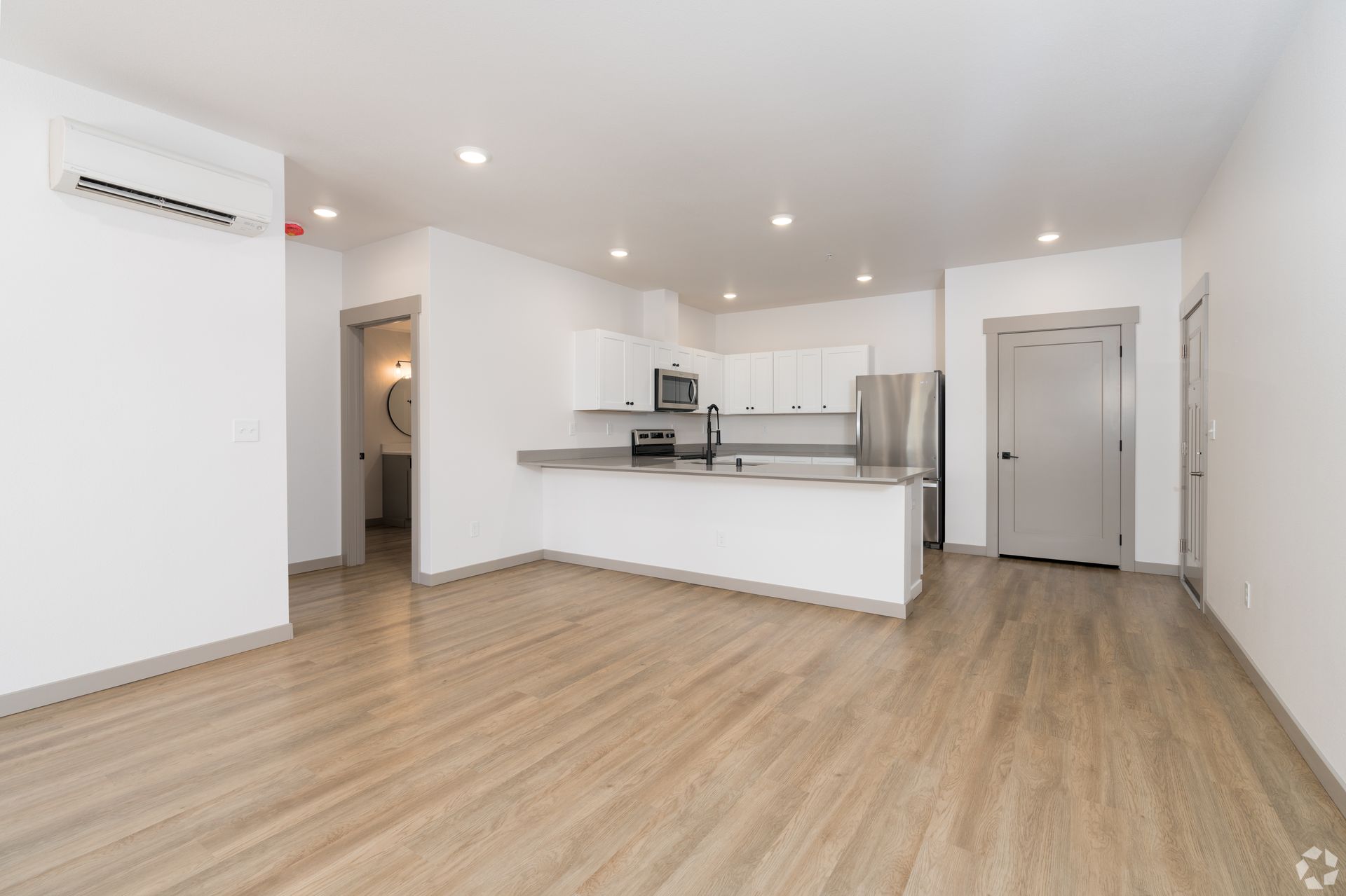 A living room with hardwood floors and a kitchen in the background.