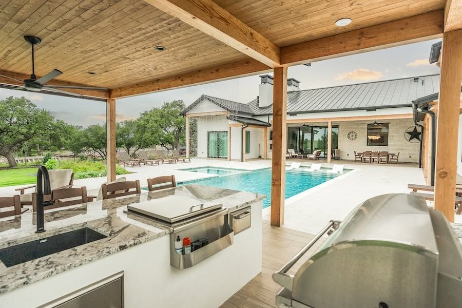 Covered patio with grill, seating, and pool overlooking a modern house and yard