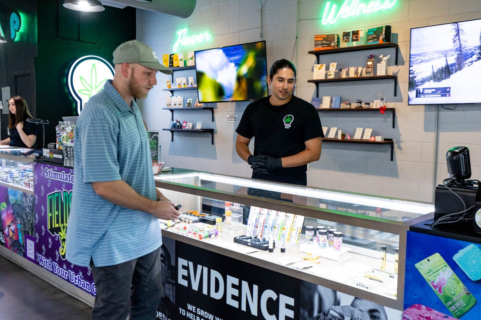 A customer at a dispensary looks at products. A staff member stands behind a display case.