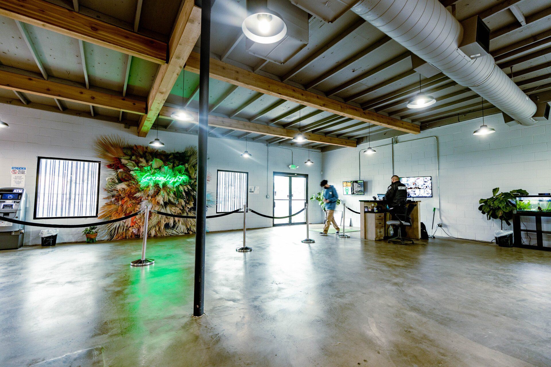Spacious industrial-style gallery. People interact near a front desk, art, and an aquarium. Fluorescent green lighting accents the space.