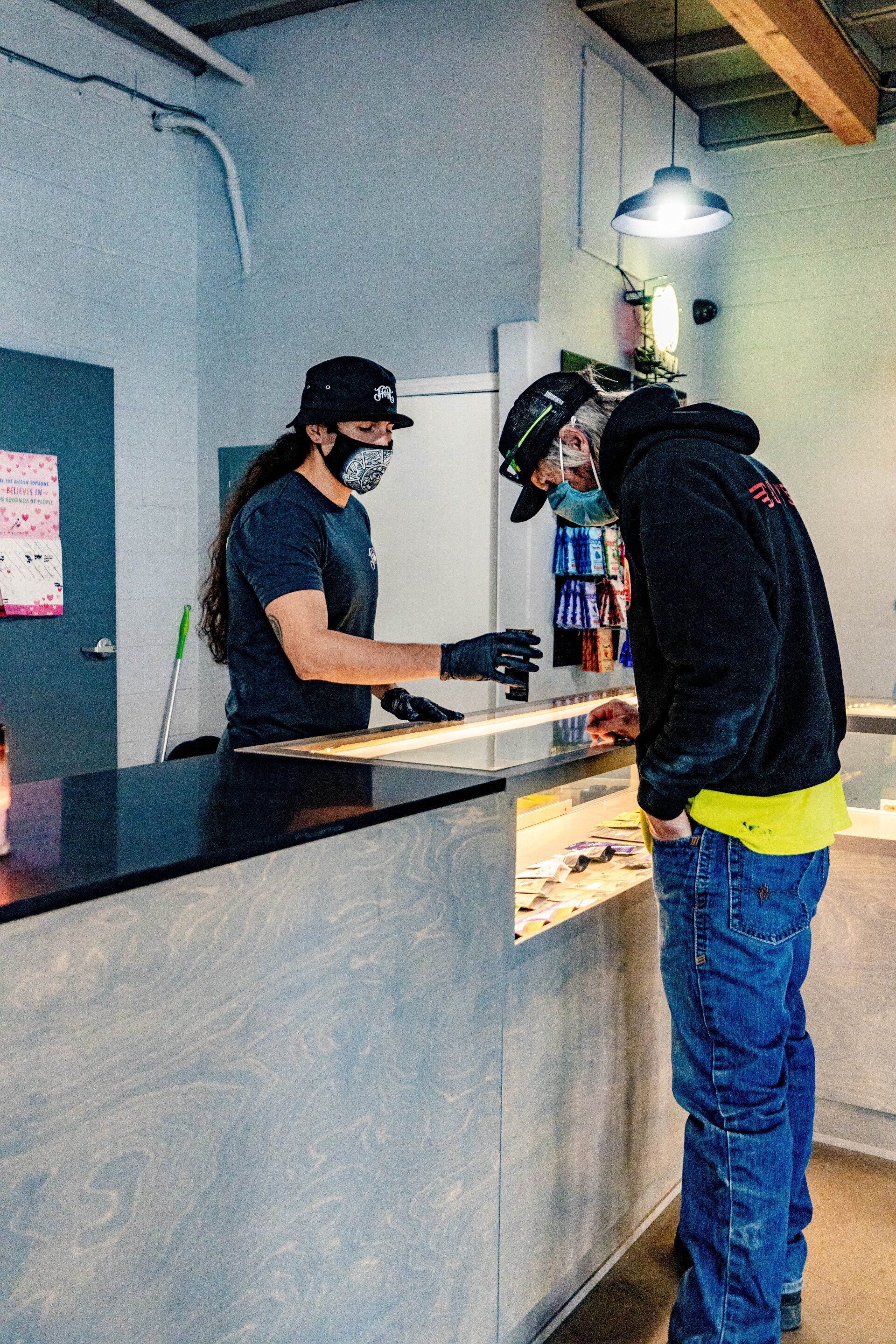 A person at a counter is being helped by a worker, both wearing masks. The setting is likely a store.
