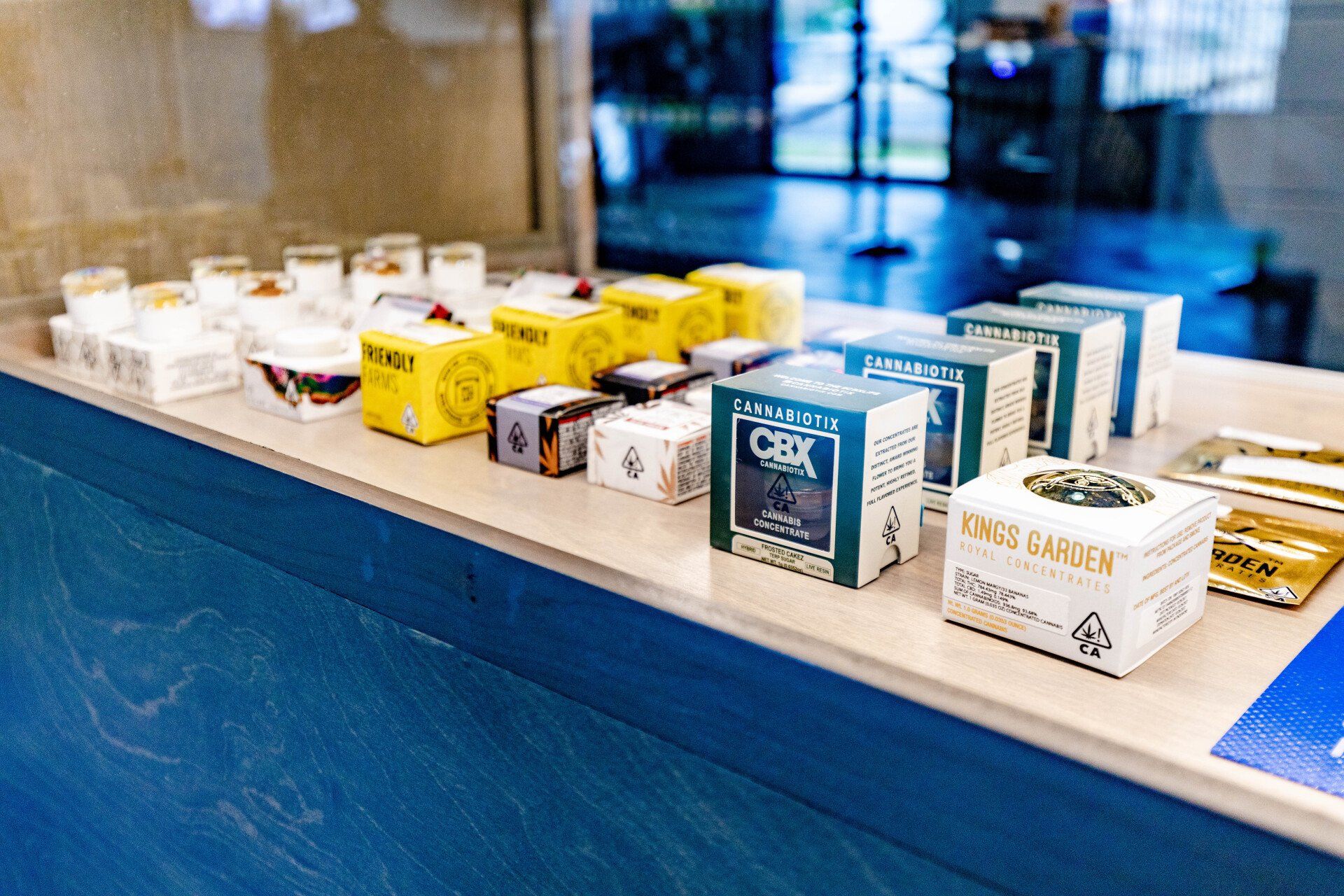 Display of packaged cannabis products on a counter in a dispensary; blue and yellow packaging.