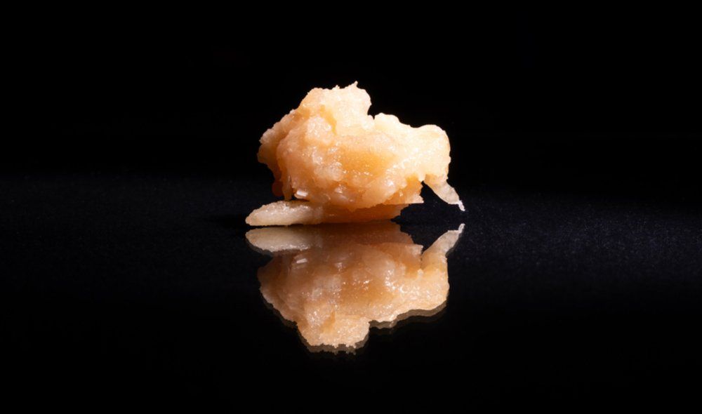 Golden brown cannabis concentrate with reflection on black surface.