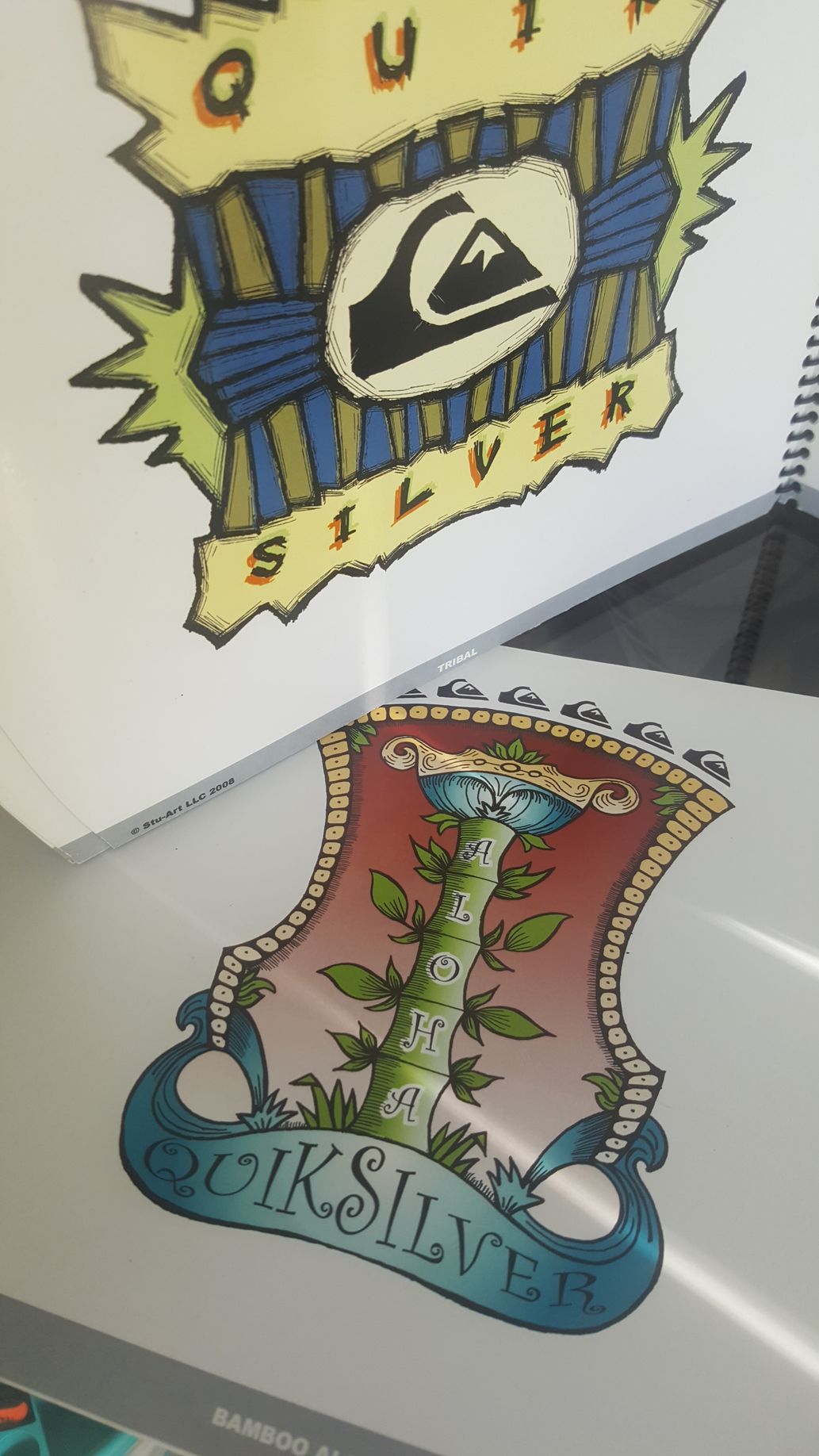 Two Quiksilver brand logos, one on a vertical binder and one printed on a flat surface below it.