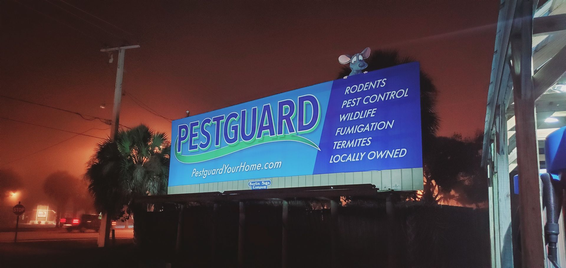 A large blue billboard for pestguard is lit up at night.