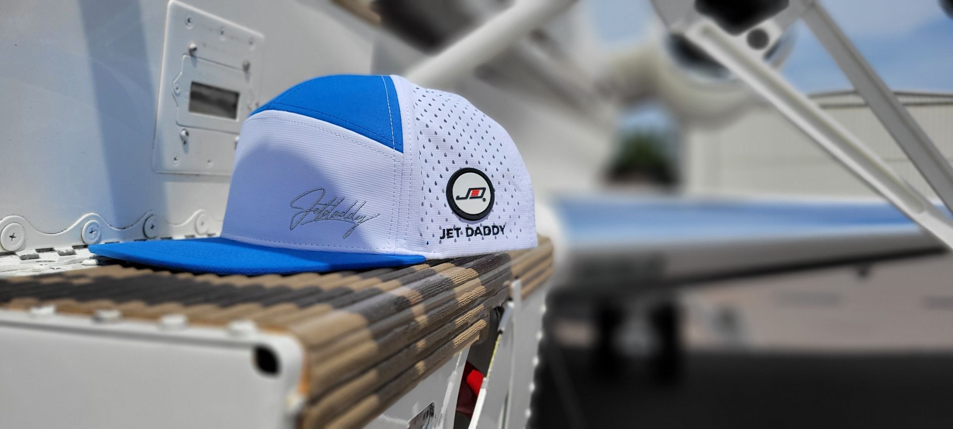 Blue & white trucker style flat bill cap sitting on a private jet entrance step.